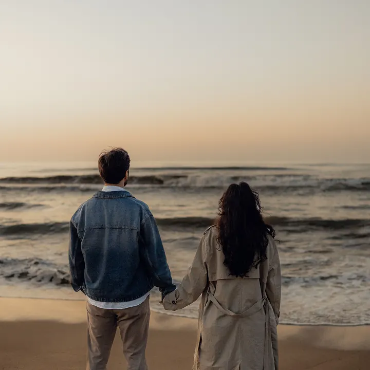 A couple holding hands, looking out at the sea at sunset
