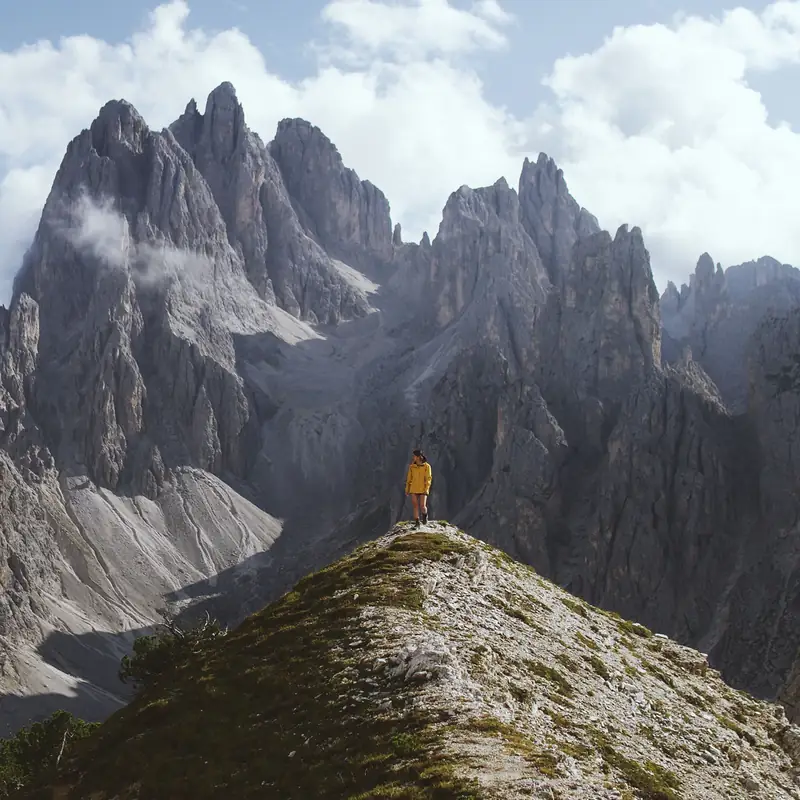 A lone hiker in a yellow jacket standing on a mountain ridge